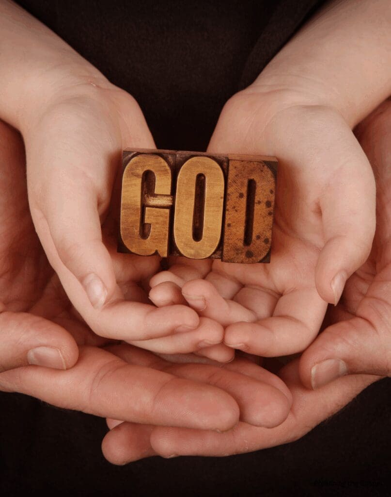 Hands holding a wooden block with the word 'GOD'.