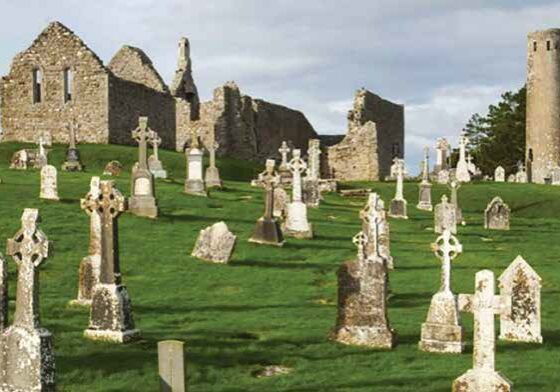 Ruins and gravestones in a grassy cemetery.