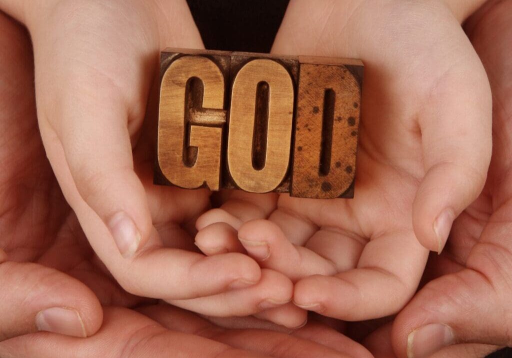 Hands holding a wooden block with the word 'GOD'.