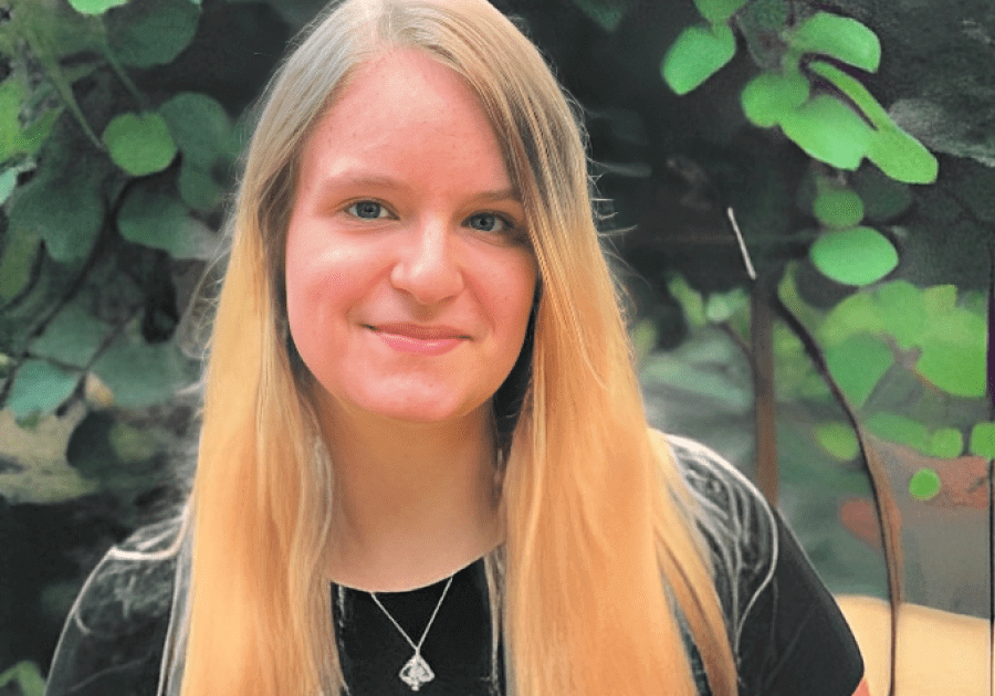 Smiling woman with long hair, leafy background.