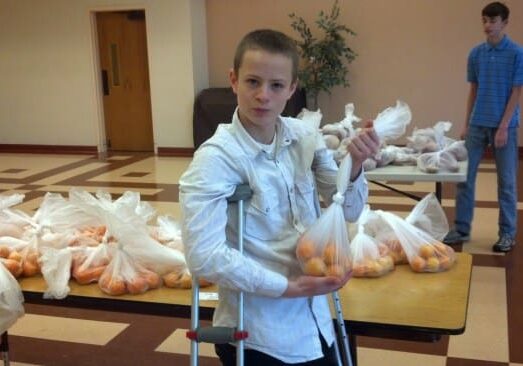 Teen on crutches holding bag of oranges