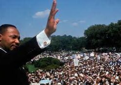 Man in suit waving to large outdoor crowd